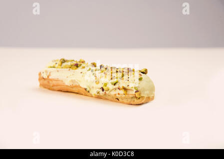 Nahaufnahme von Eclair mit weißer Creme und Muttern über Weiß isoliert Stockfoto