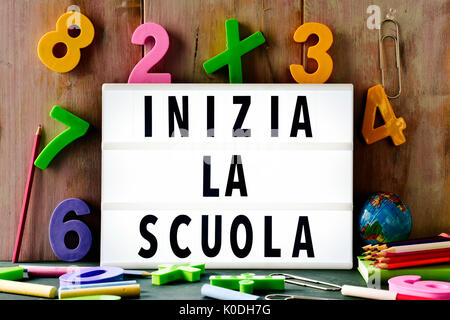 der Text Inizia la Scuola, zurück zur Schule in Italienisch, in einer Lightbox platziert vor einem rustikalen hölzernen Hintergrund, umgeben von dreidimensionalen Zahlen Stockfoto