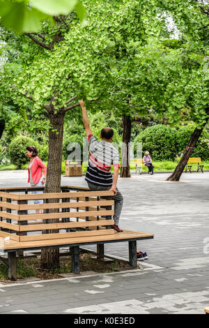 Ein chinesischer Mann war Stretching seinen Arm mit einem Ast in einem öffentlichen Park Stockfoto