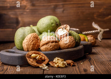 Eine Handvoll grüne junge Walnüsse auf einem hölzernen Hintergrund zusammen mit einem alten Nussknacker. Muttern mit Shell und Walnüsse in der Green Peel. Stockfoto