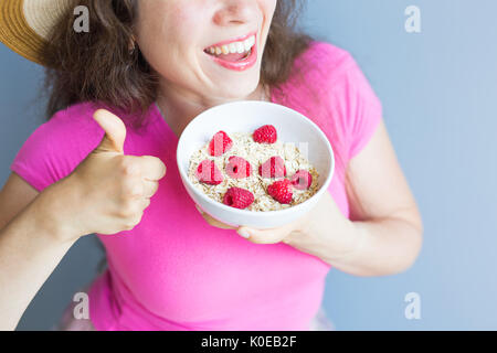 Lächelnde Frau halten gesund und natürlich Frühstück, Haferflocken und Himbeeren in eine Schüssel geben Stockfoto