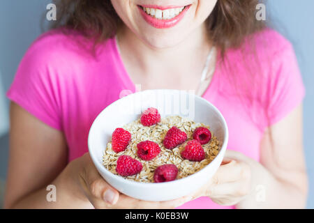 Frauenhand halten gesund und natürlich Frühstück, Haferflocken und Himbeeren in eine Schüssel geben Stockfoto