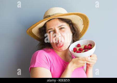 Lächelnde Frau halten gesund und natürlich Frühstück, Haferflocken und Himbeeren in eine Schüssel geben Stockfoto