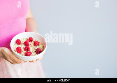 Frauenhand halten gesund und natürlich Frühstück, Haferflocken und Himbeeren in eine Schüssel geben Stockfoto