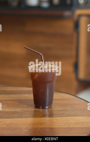 Iced Americano Kaffee in take away Becher (Glas, Kunststoff) auf dem Holz Tisch im Cafe Stockfoto