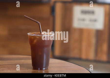 Iced Americano Kaffee in take away Becher (Glas, Kunststoff) auf dem Holz Tisch im Cafe Stockfoto