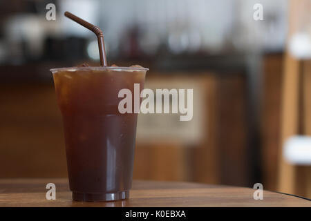 Iced Americano Kaffee in take away Becher (Glas, Kunststoff) auf dem Holz Tisch im Cafe Stockfoto