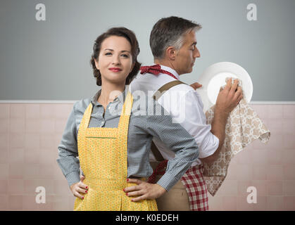 Lächelnd starke Frau, die gerade ihren Mann in Schürze Reinigung Geschirr Stockfoto