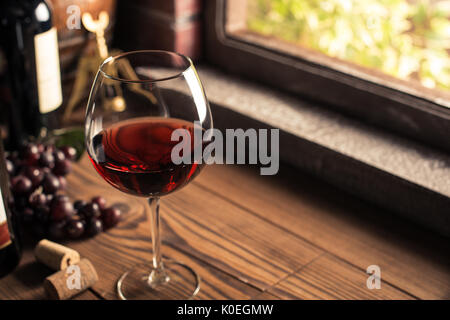 Köstliche rote Weinprobe im Weinkeller, Wein Glas und Flasche neben einem Fenster und üppigen Weinreben auf dem Hintergrund Stockfoto