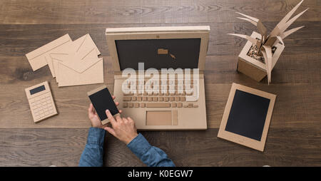 Unternehmer, die in einem kreativen umweltfreundliche Büro aus Karton, er ist mit einem Laptop und einem Smartphone, Ansicht von oben Stockfoto