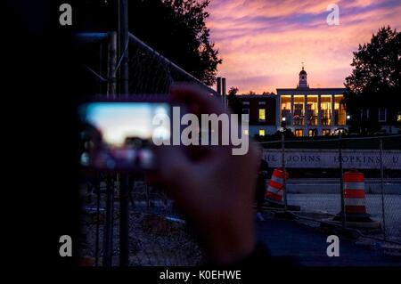 Der Hintergrund des Wegs der Johns Hopkins University und der Milton S. Eisenhower Library bei Sonnenuntergang mit einem violetten und rosa getrübten Himmel, mit dem Vordergrund eines Studenten, der sein iPhone benutzt, um ein Landschaftsfoto des Himmels an der Johns Hopkins University, Baltimore, Maryland, 7. Oktober 2013 zu machen. Mit Freundlicher Genehmigung Von Eric Chen. Stockfoto