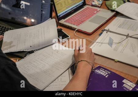 Eine Nahaufnahme eines Studenten, der die Hausaufgaben von Calculus an einem Tisch überprüft, nur ihr Arm und ihre Hand sichtbar, mit einem weiteren Satz Notizen aus einem Calculus-Lehrbuch rechts, Und ein Laptop hinter jedem Stapel von Studienmaterialien, mit Mobiltelefonen und Notebooks über den Tisch verteilt, Johns Hopkins University, Baltimore, Maryland, 2014. Mit Freundlicher Genehmigung Von Eric Chen. Stockfoto