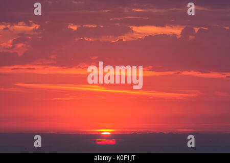 Sunrise, Sunset durch Schicht von Wolke am Horizont mit dem Meer gesehen. Stimmungsvolle sky sehr rot mit Cloud Schicht an der Spitze unter beleuchtet von der aufgehenden Sonne. Stockfoto