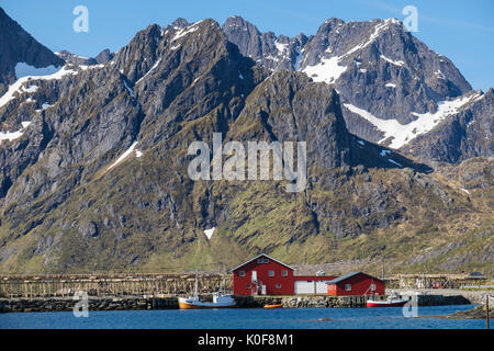 Fischerboote und Stockfisch trocknen auf Regalen unter Berge an der Küste. Sund, Insel Flakstadøya, Lofoten, Nordland, Norwegen, Skandinavien Stockfoto