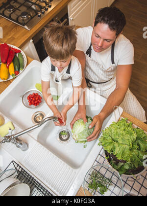 Vater mit kleinen Sohn wäscht Gemüse in der Küche vor dem Essen Stockfoto