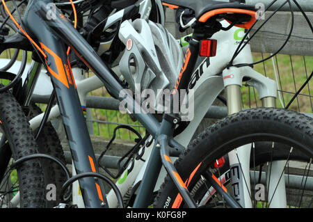 Zyklen links und gesperrt Radfahrer Fahrrad unbeaufsichtigt verlassen unter Verschluss Zyklen bei einem Zyklus rack Gefesselt für Sicherheit mit Hemet am Querträger Stockfoto