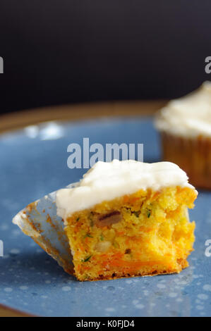 Zucchini und Karotten Cupcakes mit Philadelphia Käse Creme auf blauen Platte auf der schwarzen Oberfläche Stockfoto