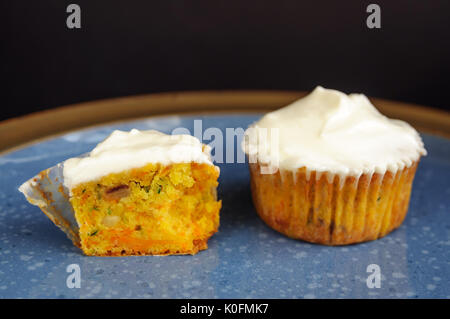 Zucchini und Karotten Cupcakes mit Philadelphia Käse Creme auf blauen Platte auf der schwarzen Oberfläche Stockfoto