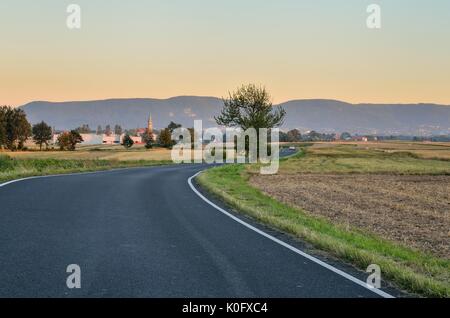 Sommer der ländlichen Landschaft. Asphaltierte Straße mit Berge und das Dorf im Hintergrund. Stockfoto