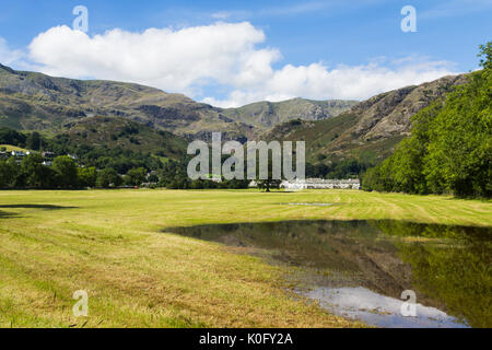 Coniston Dorf inmitten der Bäume unterhalb Coniston Fells spiegeln sich in einer ständigen Regenwasser Pool in Wiesen in der Nähe der Nordküste von Coniston Water Stockfoto