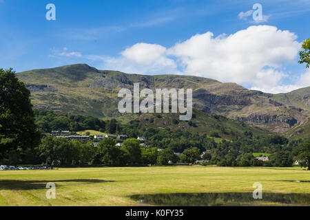 Coniston Dorf inmitten der Bäume unterhalb Coniston Fells mit dem alten Mann von Coniston steigende zu seinem 803 Meter (2.634 Fuß) Peak. Stockfoto