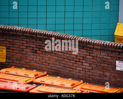 Gebogene Red brick wall hinter orange Abfallbehälter mit blau gefliesten Wand im Hintergrund in Leeds, West Yorkshire, England, Großbritannien Stockfoto