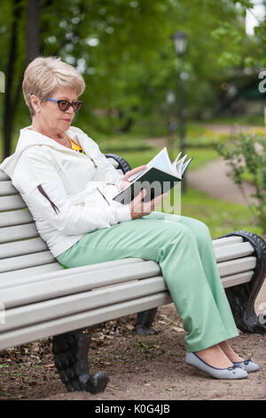 In voller Länge Porträt der älteren Frau in der Brille lesen Buch auf der Bank im Park Stockfoto