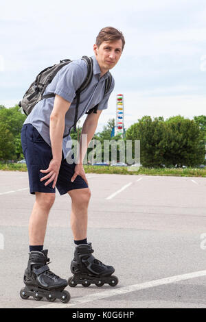 Kaukasischen Mann in Rollschuhe mit Rucksack auf Asphaltstraße, Porträt Stockfoto