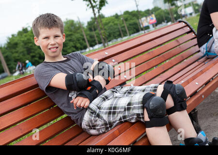 Ein zehn-jährige Junge sitzt auf einer Bank in Schutzausrüstung Inline Skates Stockfoto