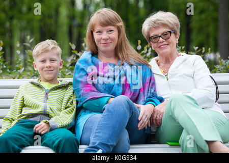 Neun Jahre odl Junge mit einer älteren Großmutter und eine junge Mutter auf einer Parkbank Stockfoto