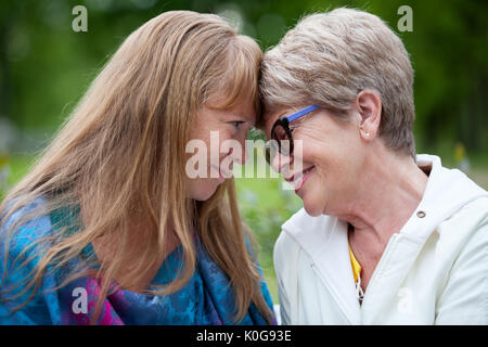 Reife Mutter und erwachsene Tochter sitzen ihre Köpfe gegeneinander gelehnt Stockfoto