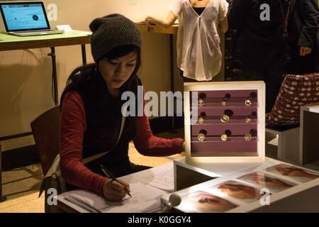 Ein Student auf einem Stuhl an einem Tisch, das Kunstwerk auf ihm sitzt, ist sie das Ausfüllen der Ausstellung Übersicht am Entwirren der Code Öffnung an der Johns Hopkins Universität Sheridan Bibliotheken, 2016. Mit freundlicher Genehmigung von Eric Chen. Stockfoto