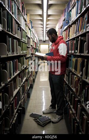 Ein Student steht und liest ein Buch unter den Stapeln in der Milton S. Eisenhower Library auf dem Homewood Campus der Johns Hopkins University in Baltimore, Maryland, 2015. Mit Freundlicher Genehmigung Von Eric Chen. Stockfoto