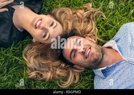 Glücklich lächelnde Paar Entspannende auf grünem Gras. Park. Junges Paar Liegen auf Gras im Freien. Elegant gekleidet Stockfoto