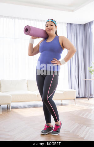 Junge lächelnde fette Frau mit einer Rolle von Mat posing Stockfoto