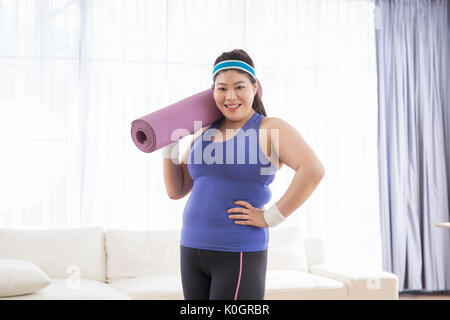 Junge lächelnde fette Frau mit einer Rolle von Mat posing Stockfoto