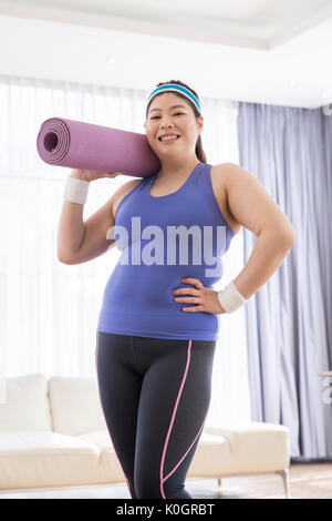 Junge lächelnde fette Frau mit einer Rolle von Mat posing Stockfoto