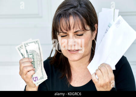 Eine Frau mittleren Alters, die Aussagen von Rechnungen und die US-Währung mit den Augen in der Frustration geschlossen Stockfoto