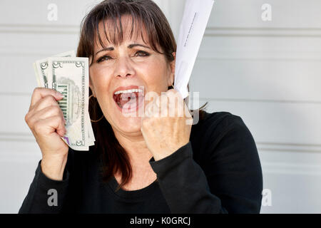 Eine Frau mittleren Alters, die Aussagen von Rechnungen und die US-Währung mit einem Umkippen, schreien Ausdruck Stockfoto