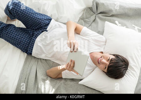 Lächelnd einzelner Mann mit Tablet liegend auf dem Bett Stockfoto