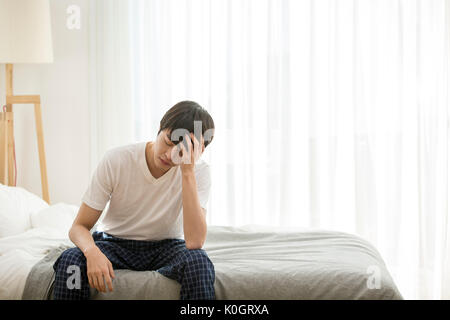 Single Mann mit Kopfschmerzen sitzen auf dem Bett Stockfoto