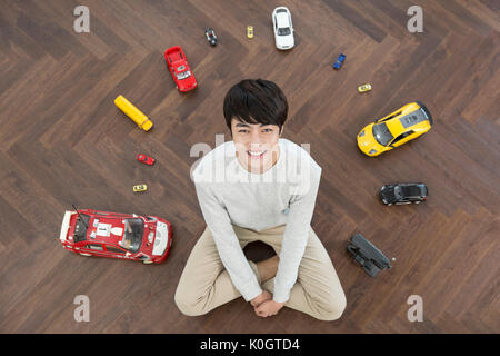 Hohe Betrachtungswinkel von lächelnden Mann kidult nach unten, die da oben sitzen, mit Spielzeugautos Stockfoto