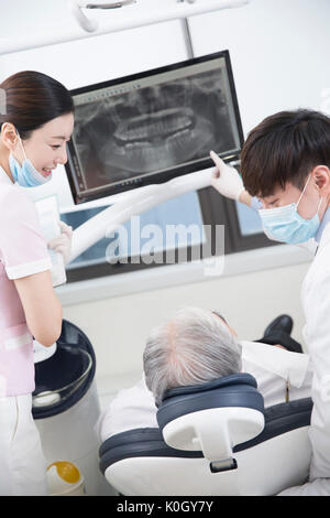 Lächelnd Zahnarzthelfer und Zahnarzt zeigt ein Röntgenbild zu einem älteren männlichen Patienten Stockfoto