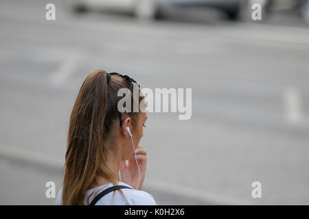 Eine junge Frau wird mit Kopfhörern bei einer Straßenbahnhaltestelle am 19 August, 2017 gesehen. Stockfoto