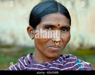 Indische Adivasi-Marktfrau mit drei goldenen Nasenringen, markanten Stammesohrringen und einem roten Bindi auf der Stirn posiert für die Kamera. Stockfoto