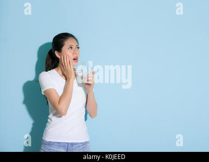 Ziemlich elegante Frau mit Eiswasser hand auf empfindliche Zähne teil und Suchen im leeren Bereich über die Lösung der blauen Wand Hintergrund denken Stockfoto