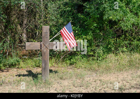 Straßenübergang-Denkmal für einen verkehrsbedingten Tod mit zwei kleinen amerikanischen Flaggen und zwei Sporen, die auf einer ländlichen Landstraße von Alabama angebracht sind. Stockfoto