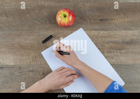 Weibliche Hände halten Füllfederhalter und ein leeres Stück Papier closeup auf hölzernen Tisch mit roten Apfel Stockfoto