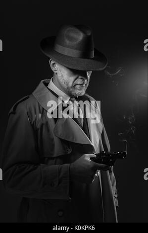 Detektiv Besitz einer Waffe, er trägt ein fedora Hut und Trenchcoat, 1950er Jahre noir Film Stockfoto