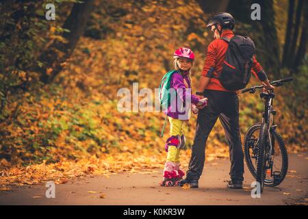Familie Outdoor Aktivitäten. Vater und Tochter im Park. Radfahren und Rollschuhe. Stockfoto